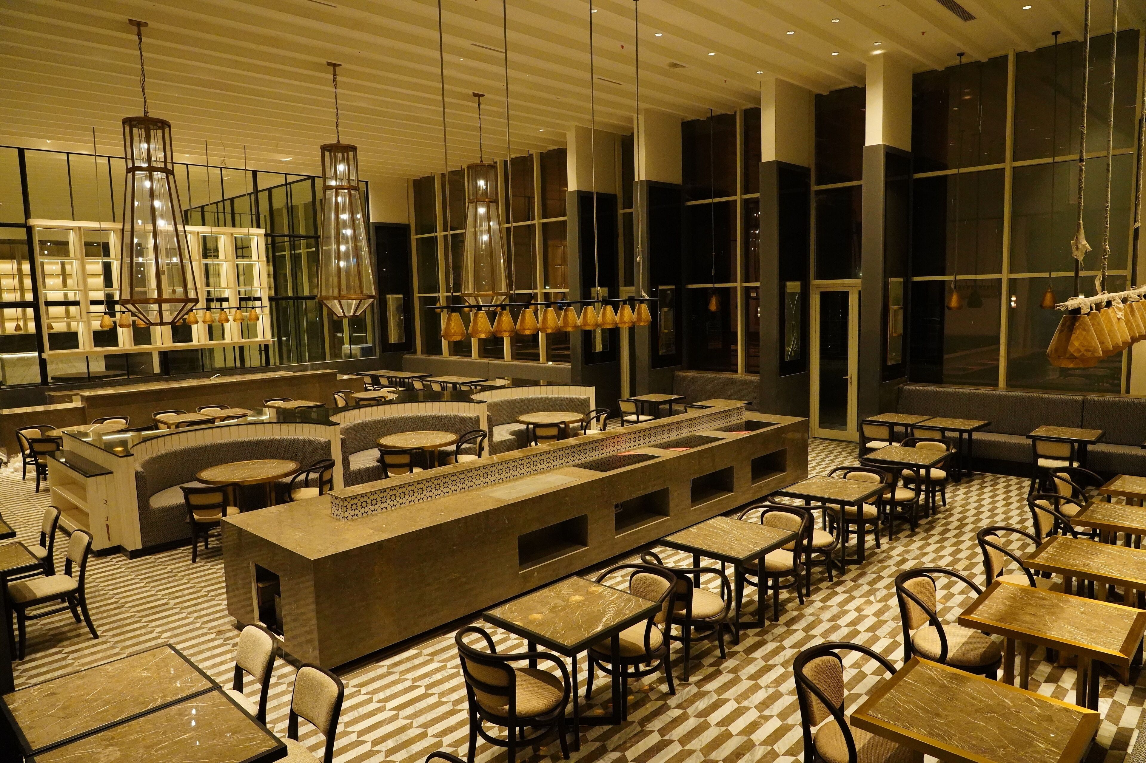 A modern restaurant with a central bar, multiple seating areas, and large windows.