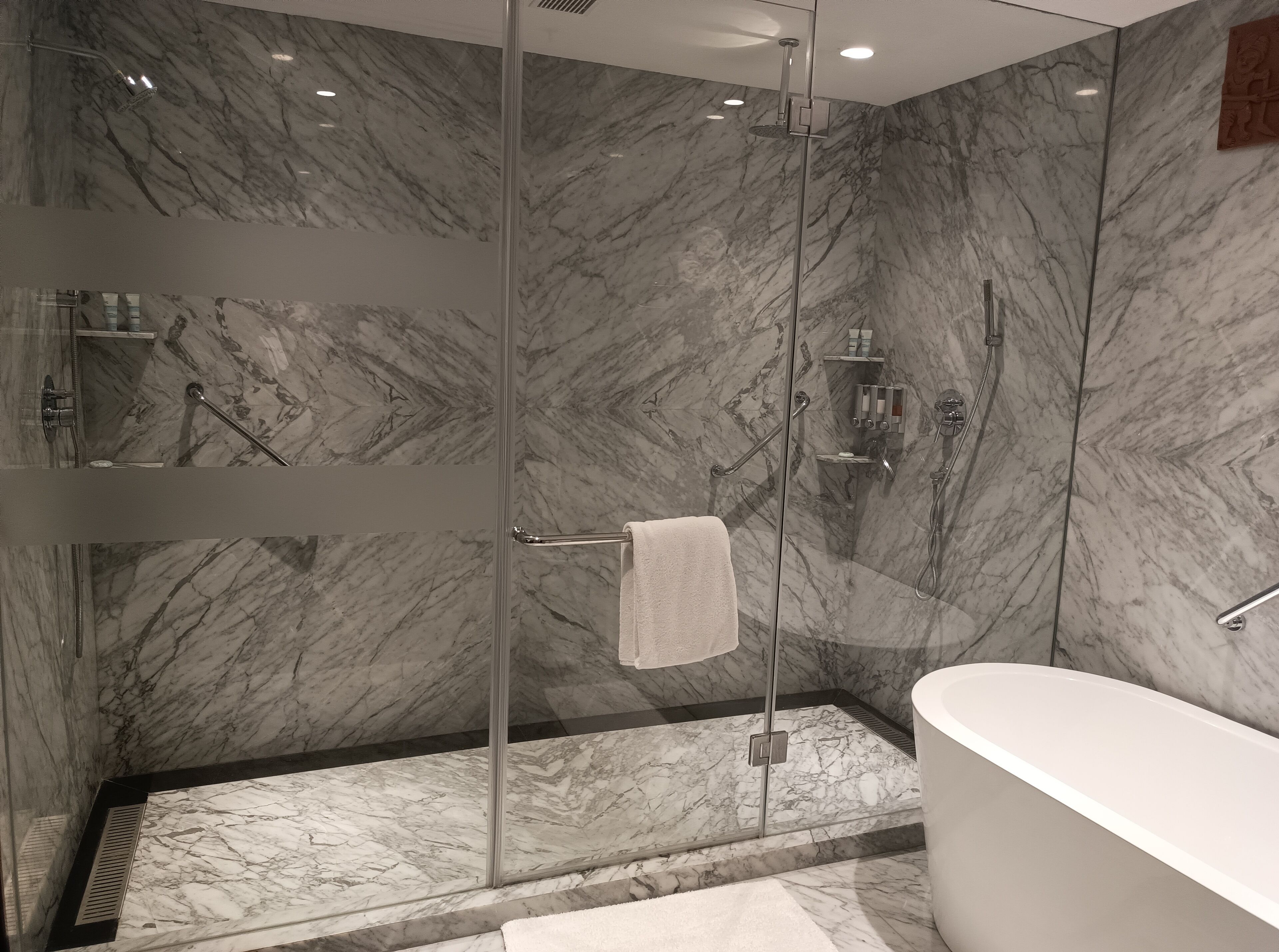 A modern bathroom with a glass-enclosed shower, a freestanding bathtub, and marble walls.
