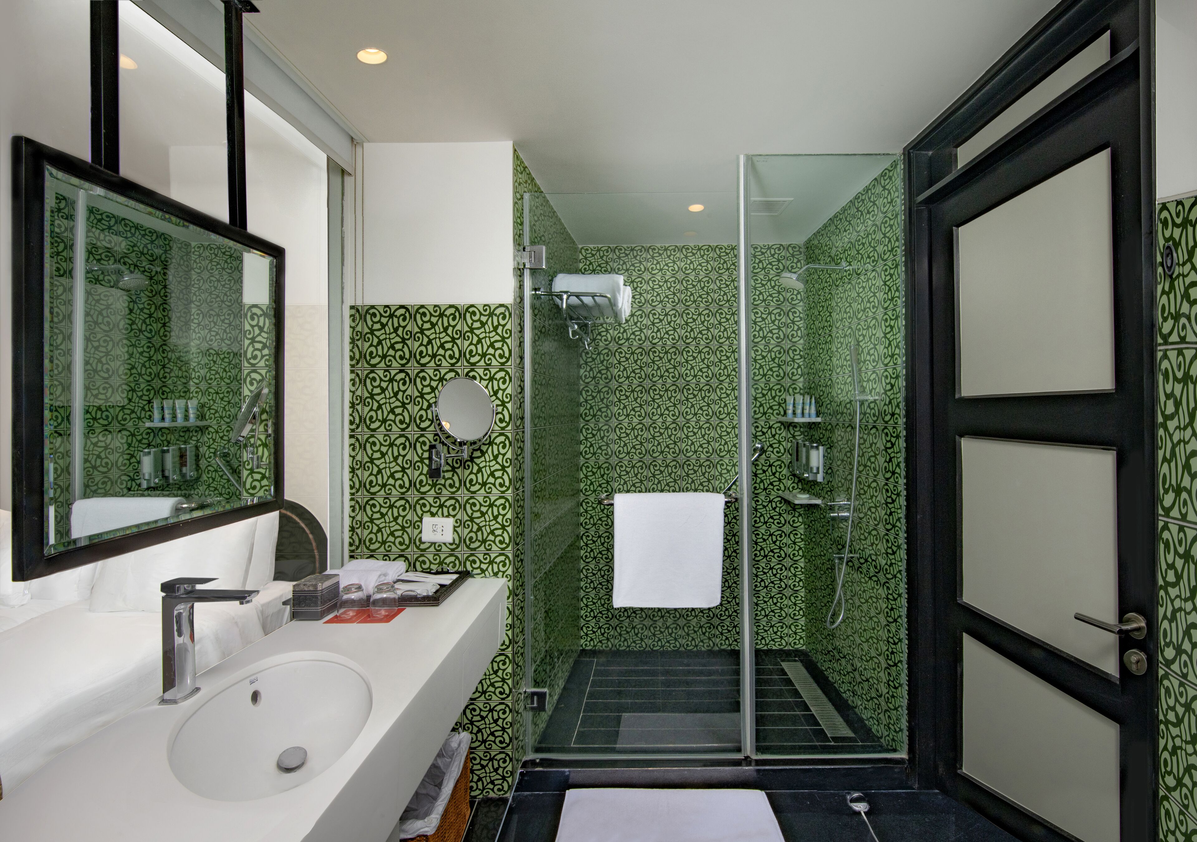 A bathroom with a white sink, a large mirror, a glass shower enclosure, and green patterned walls.