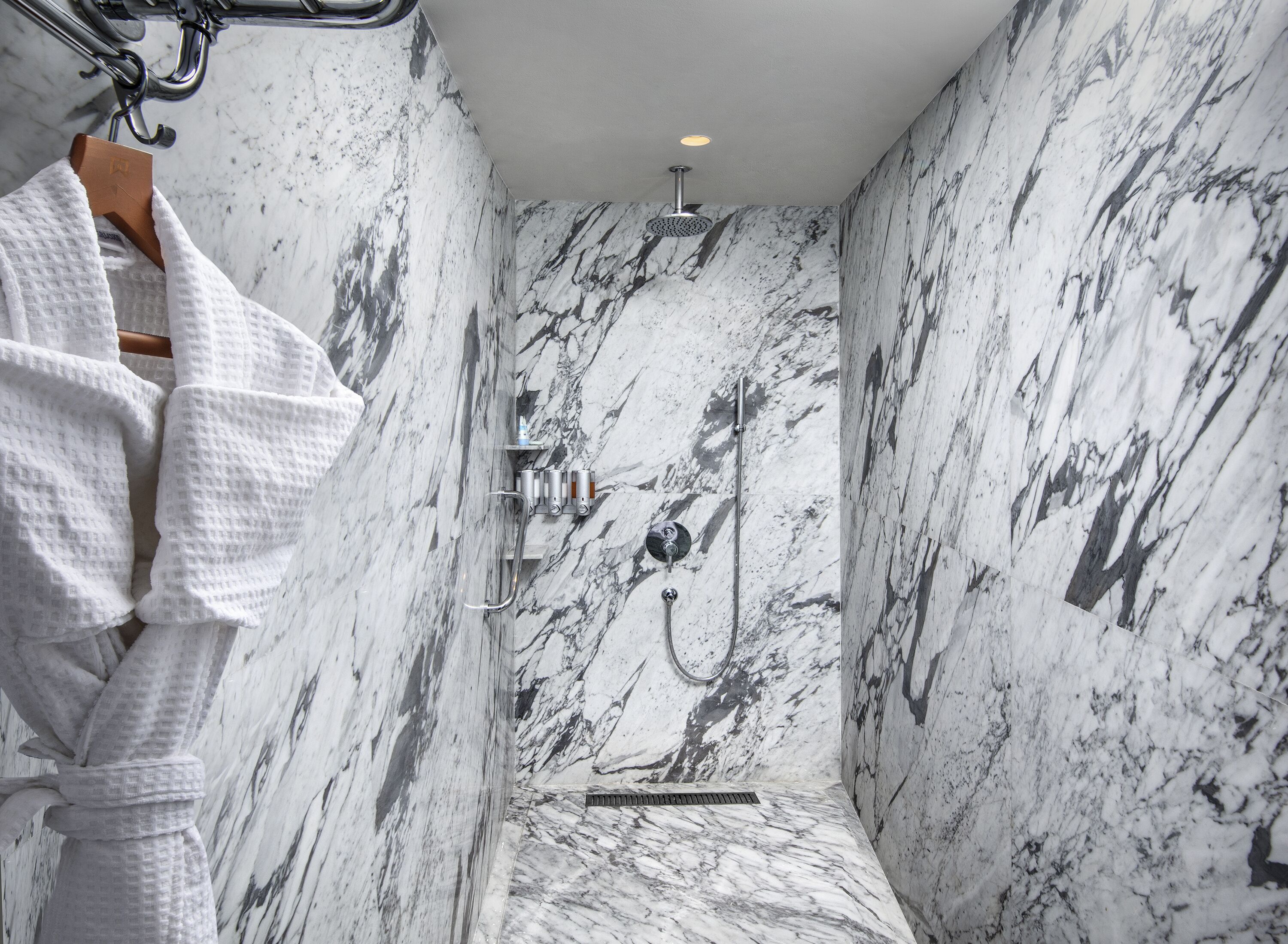 A bathroom with marble walls, a shower, and a towel rack.