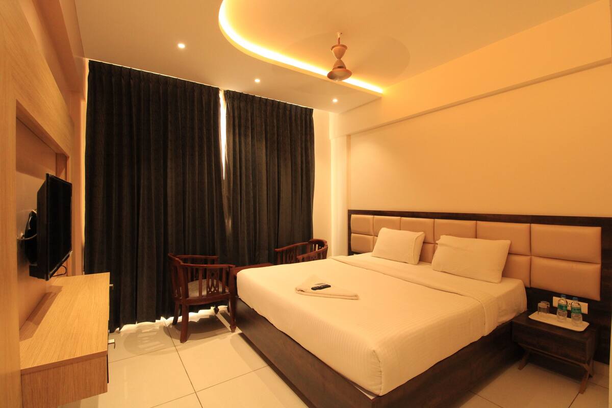 A hotel room with a large bed, a TV mounted on the wall, a desk, and a chair.