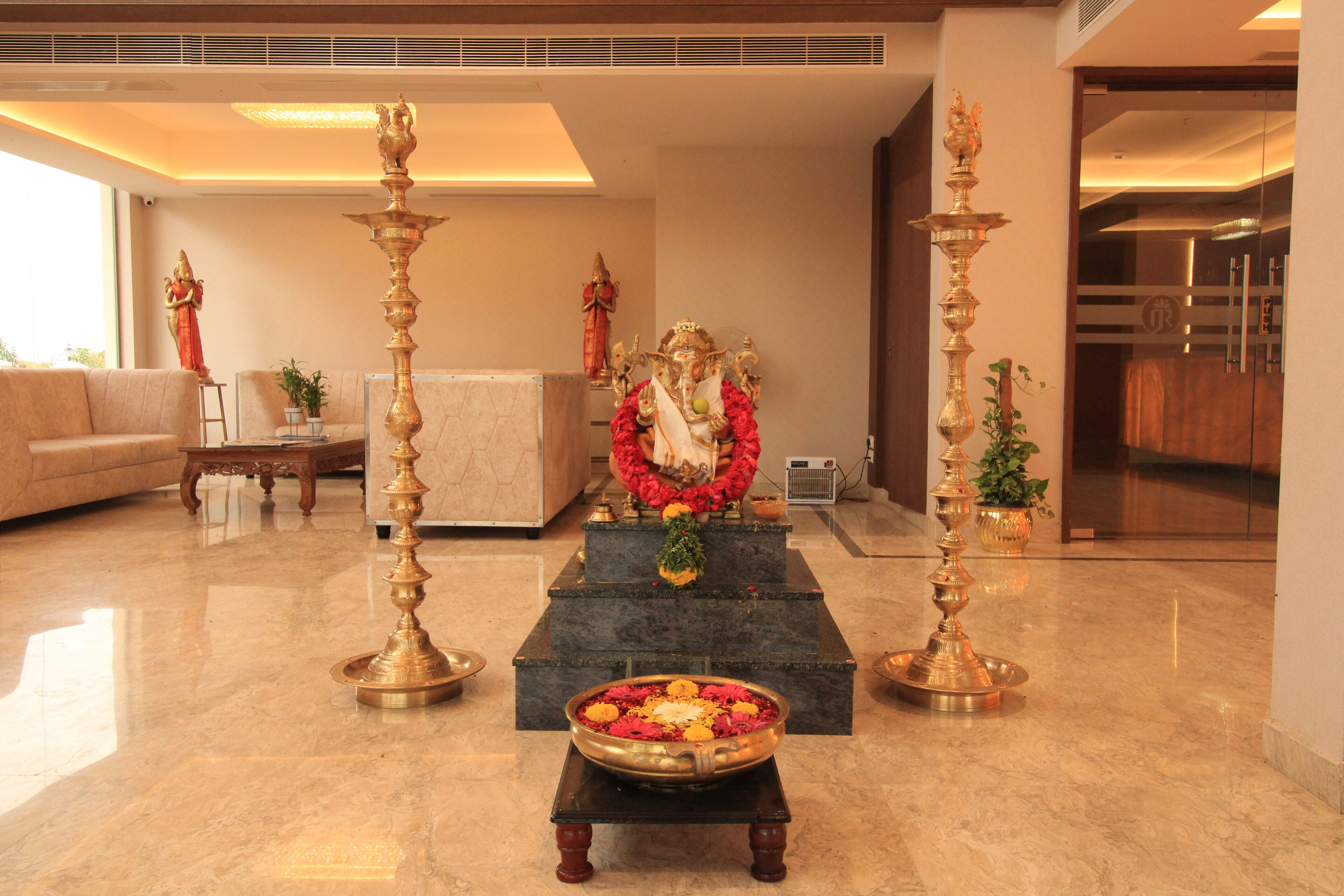 A lobby with a reception desk, sofas, and a decorative altar with flowers and a statue.