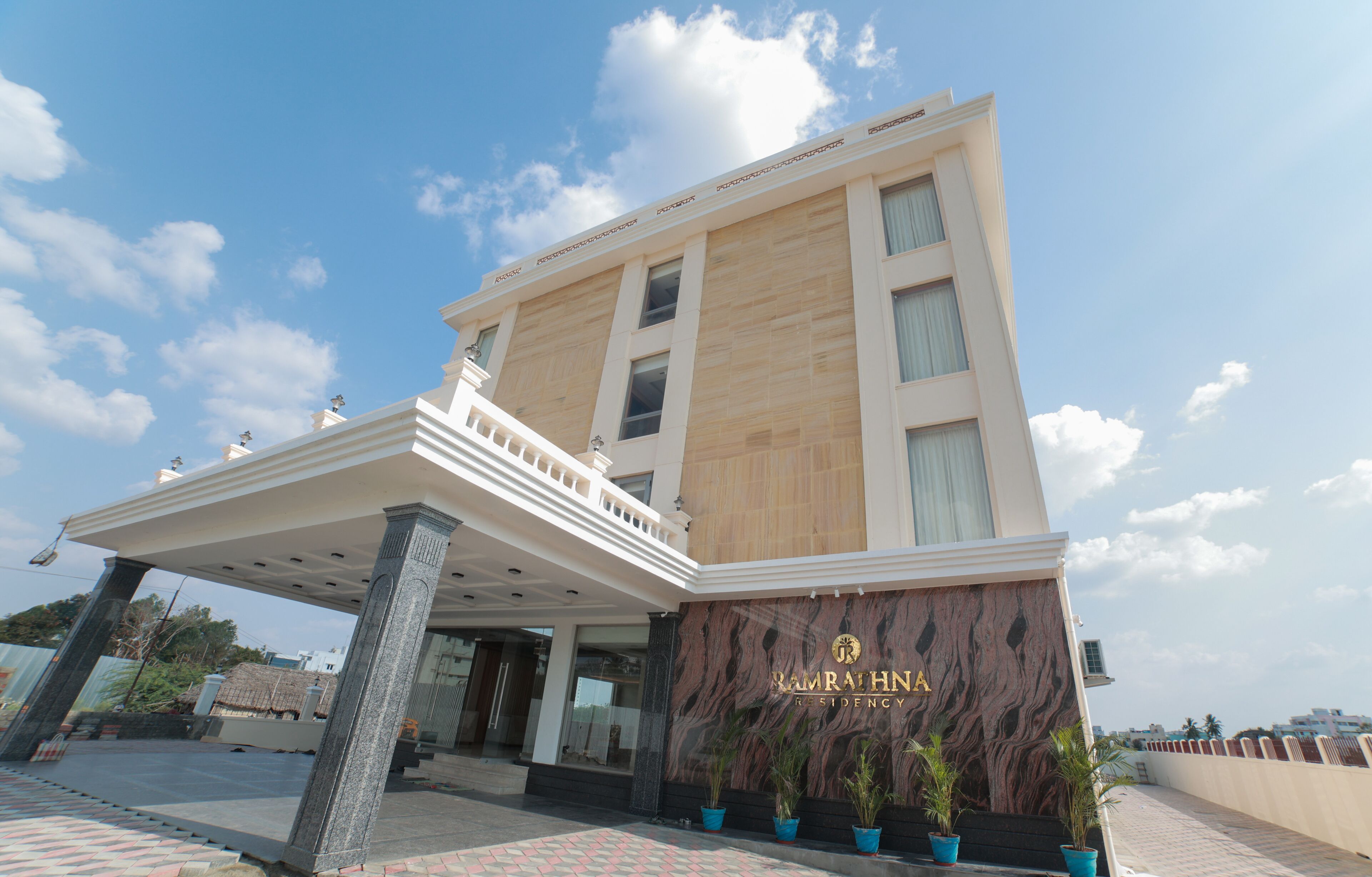Un hotel moderno con fachada de mármol, entrada cubierta y plantas en macetas.