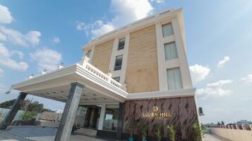 Un hotel moderno con fachada de mármol, entrada cubierta y plantas en macetas.