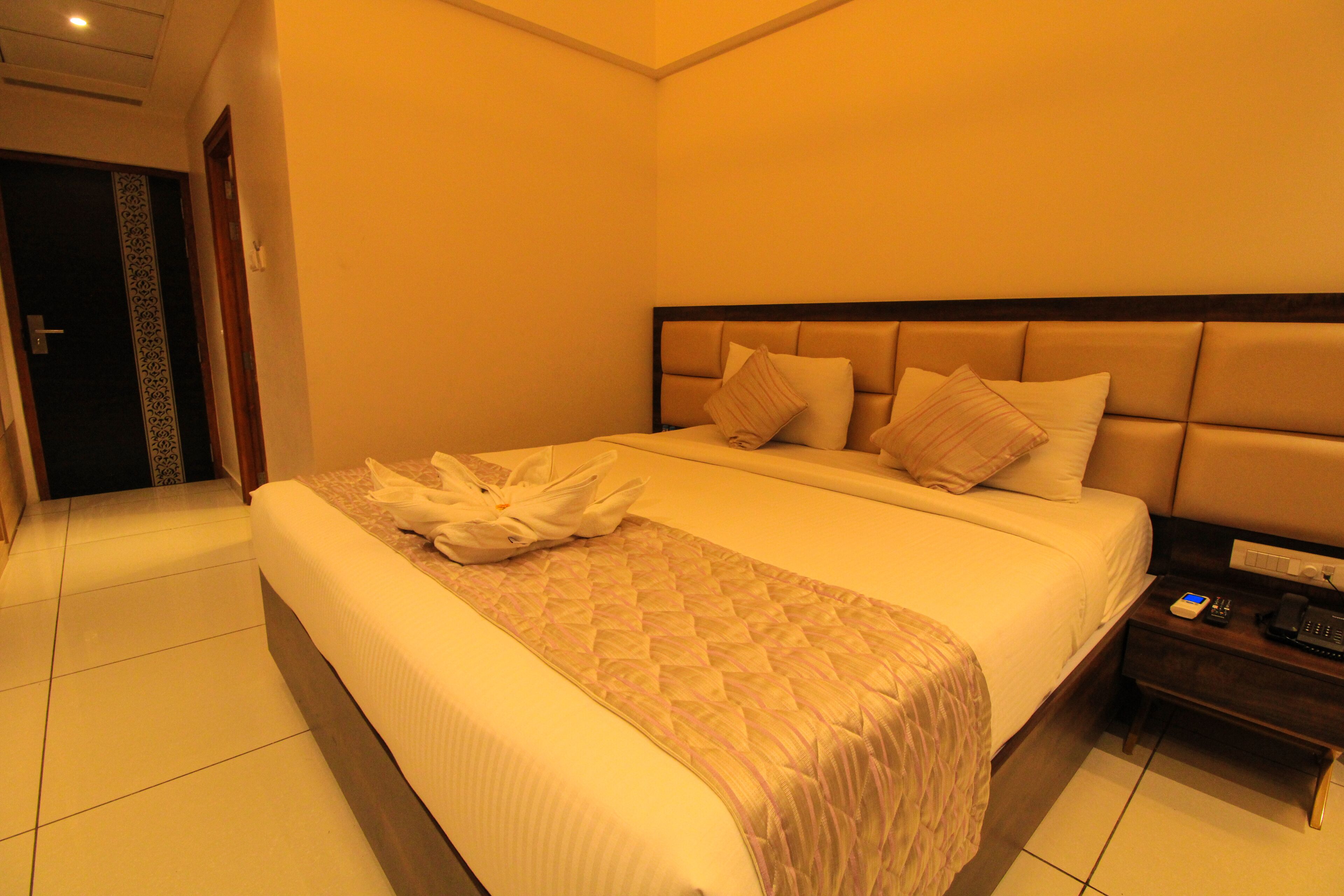 Una habitación de hotel con una cama grande, una mesita de noche con teléfono y una puerta con detalles decorativos.