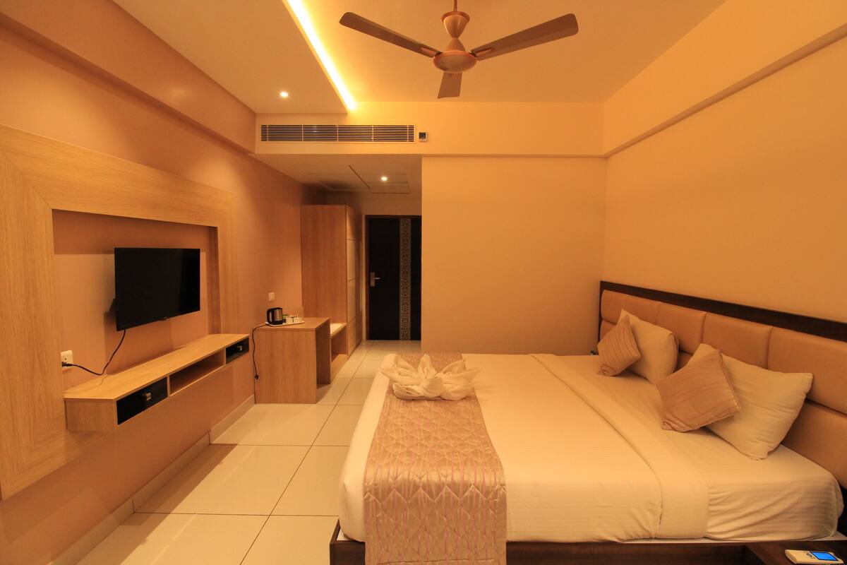 A modern hotel room with a large bed, a flat-screen TV mounted on the wall, a bedside table, and a ceiling fan.