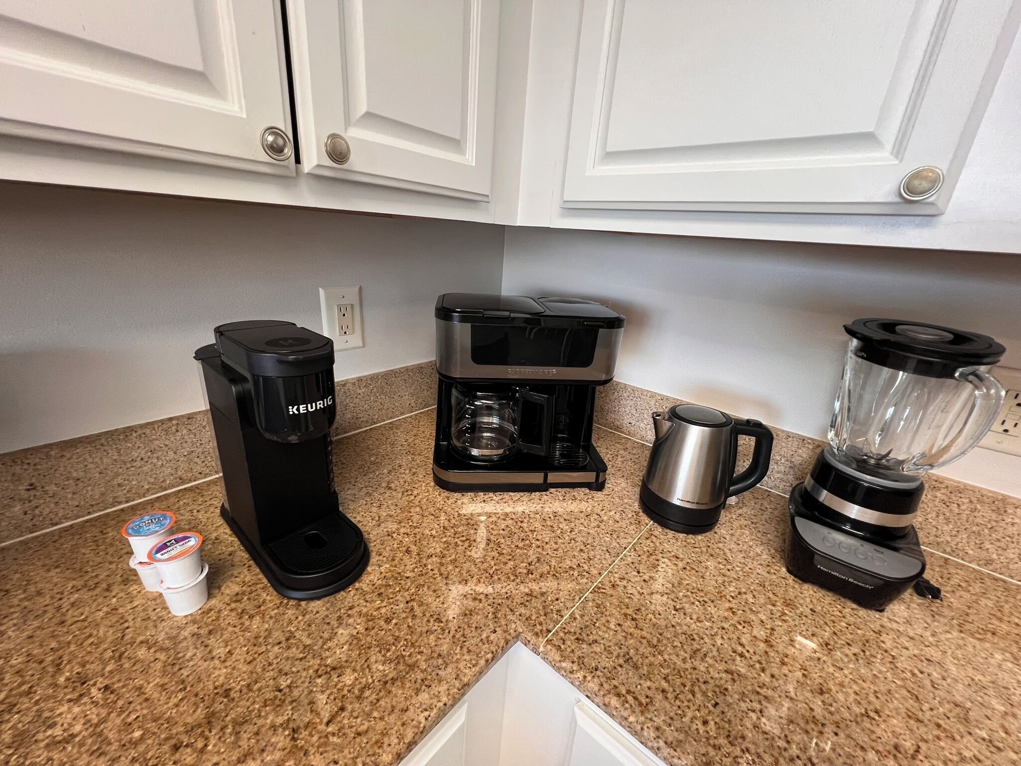 Una cocina equipada con cafetera, licuadora, hervidor y dispensador de cápsulas Keurig.