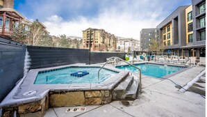 Un espace piscine aménagé sur le toit, avec un jacuzzi, des chaises longues et une vue sur les bâtiments environnants.