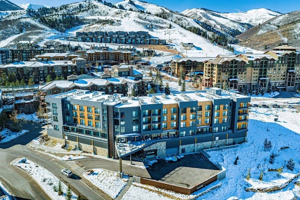 Un hôtel moderne à plusieurs étages, doté d’un parking et offrant une vue sur des montagnes enneigées.