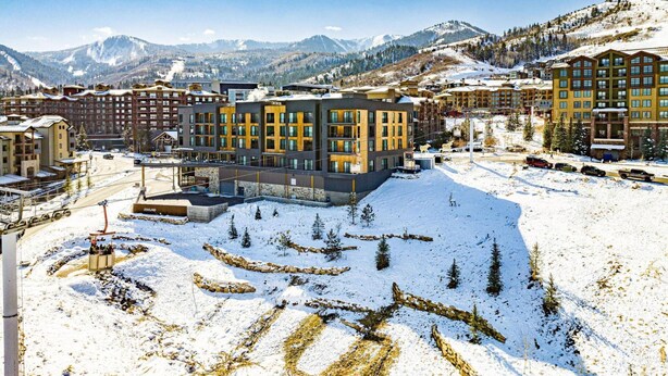 Un hôtel moderne à plusieurs étages, entouré de montagnes enneigées et situé à proximité d’une station de ski.