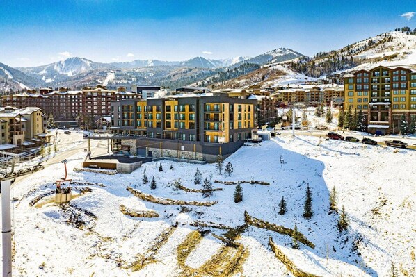 A hotel complex with multiple buildings, ski slopes in the background, and a snow-covered landscape.