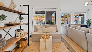 Una sala de estar moderna con un sofá color beige, estantes de madera y vista al exterior.