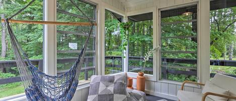 Una habitación acogedora con una hamaca, un banco acolchado y vistas al bosque.