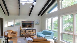 A spacious living room with a fireplace, a large window, and a view of the outdoors. - Modern Hideaway w/ Deck + State Forest Access (Parksville)