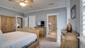 A bedroom with a bed, dresser, television, and a door leading to a bathroom.