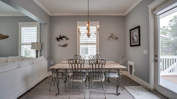 Un espace repas avec une table en bois et des chaises en métal, un lustre et des œuvres d’art décoratives accrochées au mur.