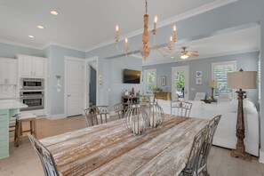 A spacious kitchen with white cabinets, a wooden dining table, and a chandelier.