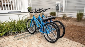 Un vélo bleu est garé sur un chemin de briques devant une maison dotée d’un porche blanc et d’un revêtement extérieur gris.