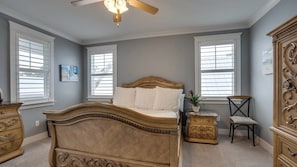 Une chambre à coucher avec un grand lit, deux fenêtres, un ventilateur de plafond et une commode.
