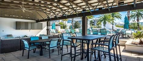 Un patio al aire libre con mesas y sillas, una zona de estar cubierta y una piscina al fondo.