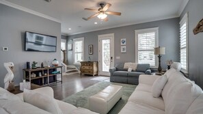 A spacious living room with a grey sofa, a white sofa, a wooden cabinet, and a ceiling fan.