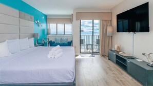 A hotel room with a large bed, a TV, a balcony with a view, and a desk with a lamp. - Palace 1501 (Myrtle Beach)