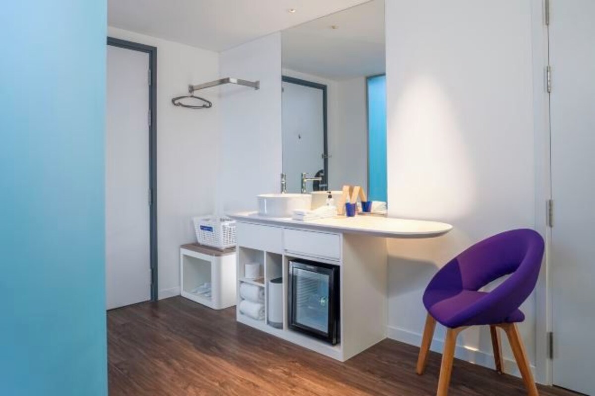 Une salle de bain moderne avec un meuble-lavabo blanc, un petit réfrigérateur et une chaise violette.
