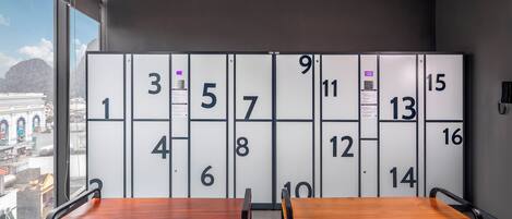 A hotel room with a large window, two wooden tables, and a wall with numbered lockers.