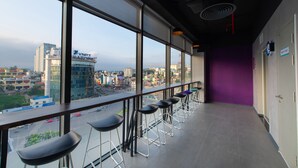 A modern bar area with high windows offering city views, a purple accent wall, and a series of bar stools. - Tru by Hilton Ha Long Hon Gai Centre (Hong Gai)