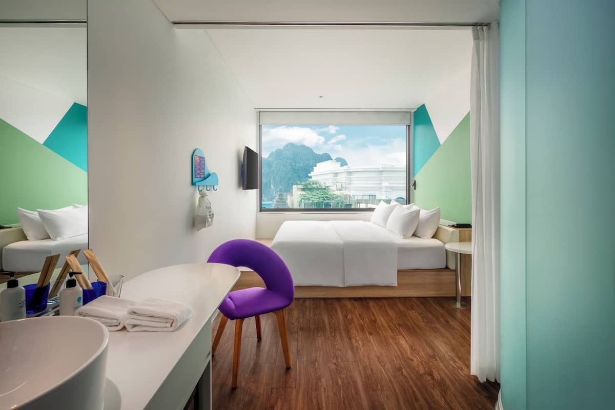 Ein modernes Hotelzimmer mit großem Fenster, einem weißen Sofa, einem violetten Sessel und Holzboden.
