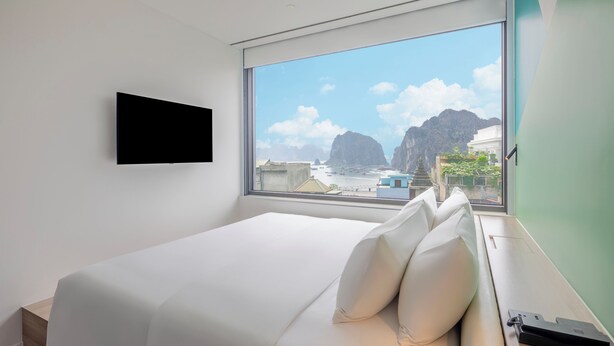 A modern hotel room with a large bed, a mounted TV, and a view of a coastal landscape. - Tru by Hilton Ha Long Hon Gai Centre (Hong Gai)