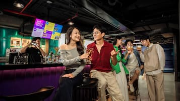 Espaço de bar com balcão, banquetes e um grupo de pessoas conversando.