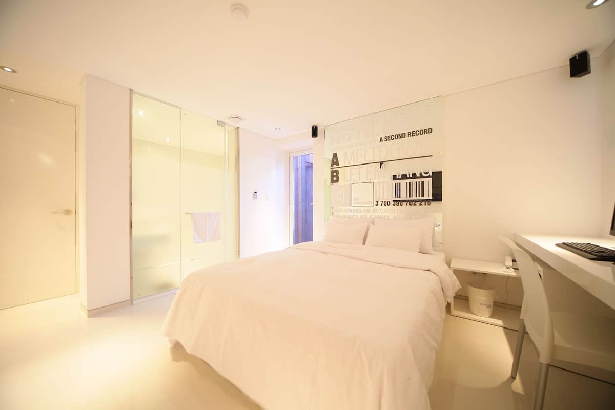 Een moderne hotelkamer met een bed, een bureau en een glazen deur naar een badkamer.