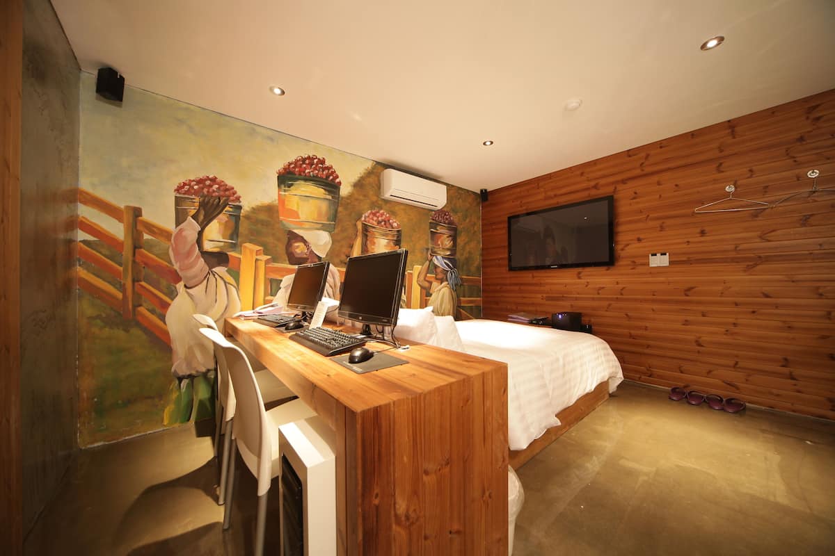 Een slaapkamer met een houten bureau, twee computers, een bed en een televisie.