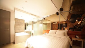Una habitación de hotel moderna con una cama grande, un baño con paredes de vidrio y una pared decorativa de ladrillo.