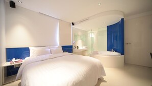 Un dormitorio moderno con una cama grande, una mesita de noche con un teléfono y libros, un escritorio empotrado y un baño con bañera y espejo.