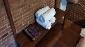Een houten bank voor een bakstenen muur, met opgerolde witte handdoeken en een kleurrijk geweven item.
