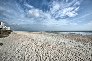 Ein Sandstrand mit Fußabdrücken, einem Holzzaun und einem Gebäude im Hintergrund.