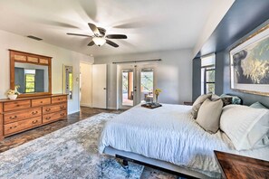 A bedroom with a large bed, wooden dresser, ceiling fan, and a view through a door to an outdoor patio. - Port Charlotte Retreat w/ Heated Pool & Spa! (Port Charlotte)