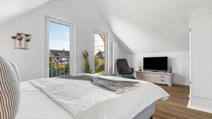 A bedroom with a large bed, a TV, and a chair. - Vacation apartment Nordseebrise in the Nordseeresort - terrace, fireplace, infrared cabin, S (Büsum)