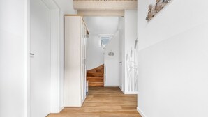A modern, minimalist hallway with wooden flooring and white walls, leading to a staircase. - Vacation apartment Nordseebrise in the Nordseeresort - terrace, fireplace, infrared cabin, S (Büsum)