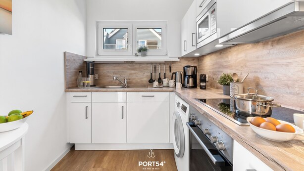 A modern kitchen with white cabinets, a wooden backsplash, and stainless steel appliances. - Vacation apartment Nordseebrise in the Nordseeresort - terrace, fireplace, infrared cabin, S (Büsum)