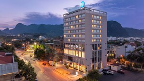 Un hotel moderno con un llamativo letrero 'TRU', rodeado de una zona urbana bien iluminada con calles visibles y montañas a lo lejos.