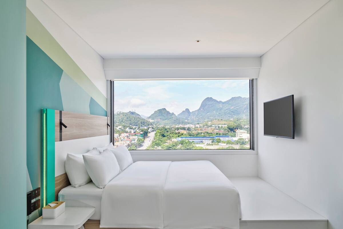 Ein modernes Schlafzimmer mit großem Fenster, einem Bett, einem Nachttisch und einem angebrachten Fernseher.