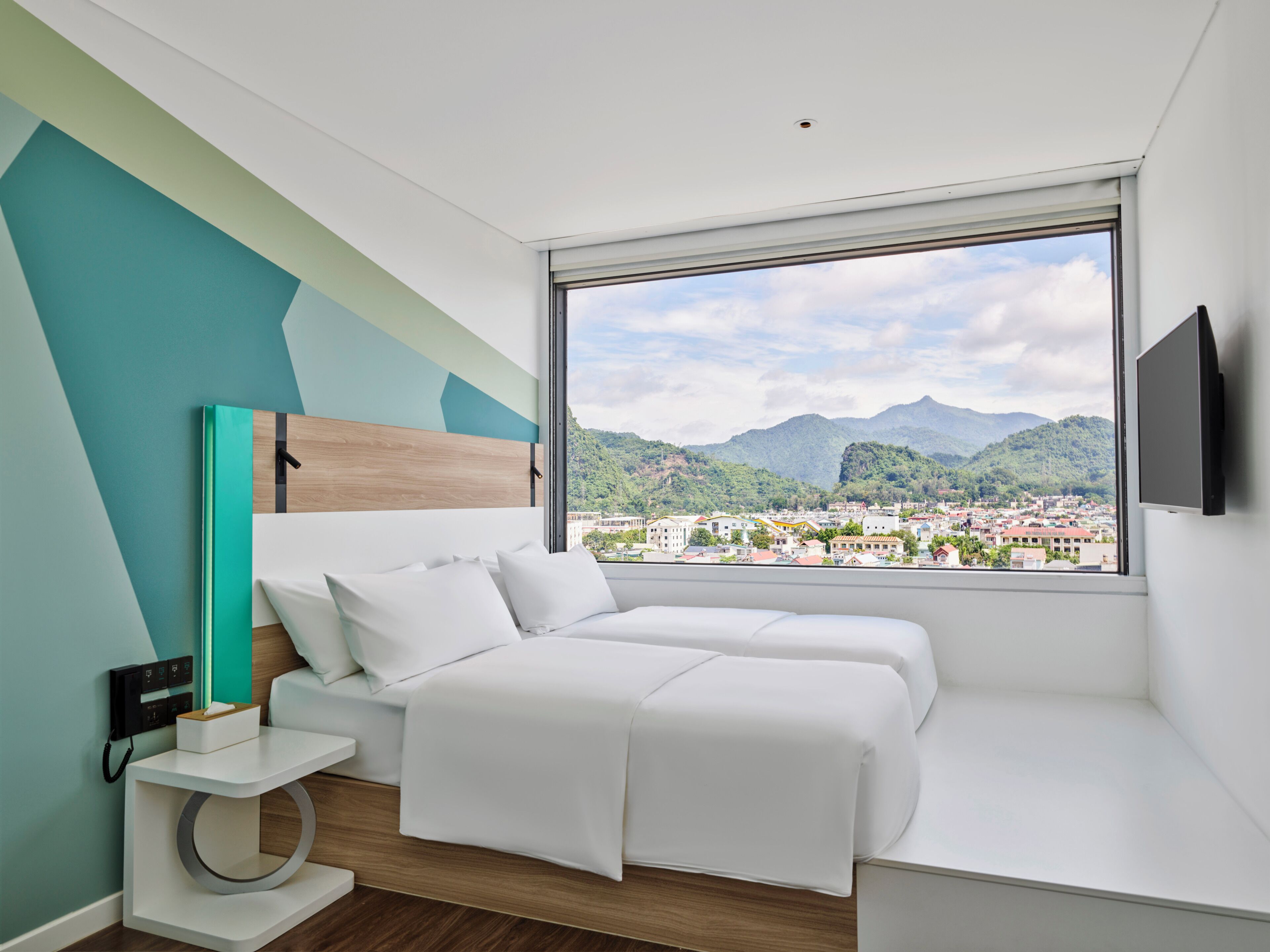 A modern bedroom with a bed, bedside table, and a large window offering a cityscape view.