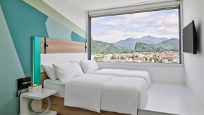 Un dormitorio moderno con cama, mesita de noche, televisor y un amplio ventanal con vistas a la ciudad.