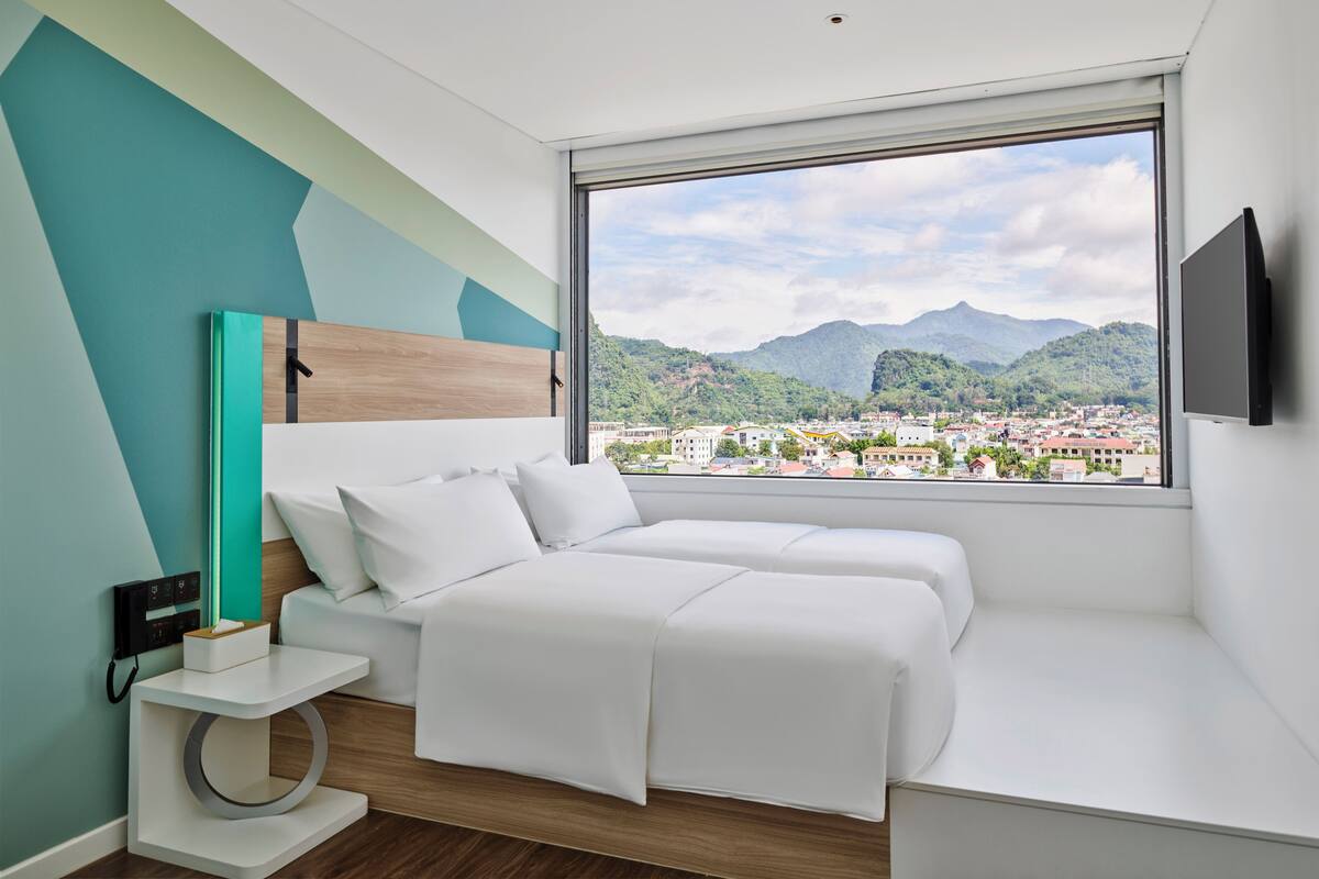 Ein modernes Schlafzimmer mit Bett, Nachttisch und großem Fenster mit Blick auf die Stadt.