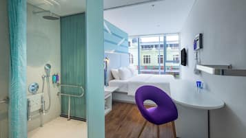 Un hotel moderno con ducha, cama, escritorio pequeño y vistas a la ciudad.