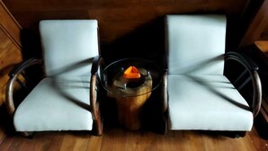 A room with two white cushioned chairs facing a round glass table with a candle. - Borobudur Balkondes Saka Pitu (Yogyakarta)