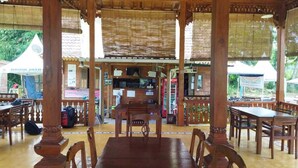 A wooden pavilion with tables and chairs, a counter, and a sign in the background. - Borobudur Balkondes Saka Pitu (Yogyakarta)